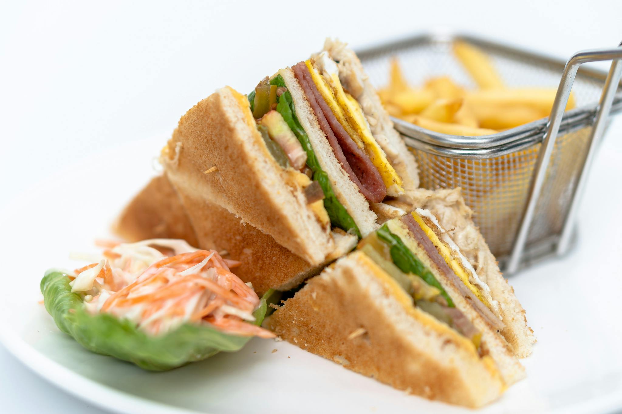 Close up of a club sandwich served with coleslaw and French fries.